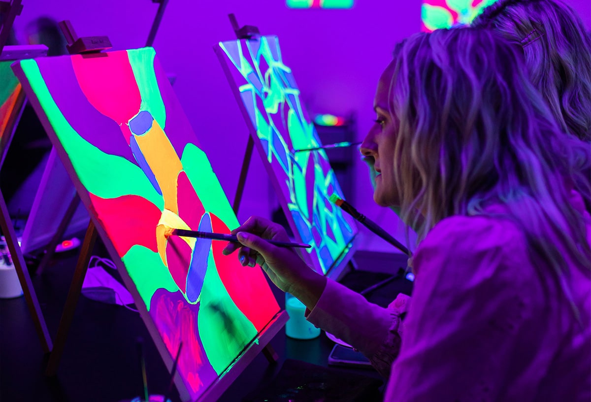 Women enjoy a Neon Nights paint and sip experience at Pinot & Picasso